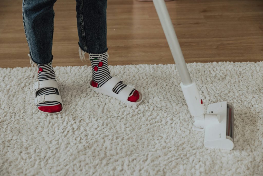 Person vacuuming white carpet in sandals